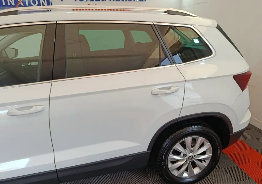 Vue latérale droite d'un Skoda Karoq blanc 2024, mettant en valeur la roue arrière et les vitres teintées.