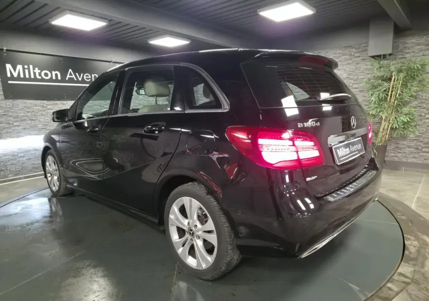 Mercedes Classe B 180d noir vue 3/4 arrière droit, feux arrière allumés et jantes alliage 17 pouces.