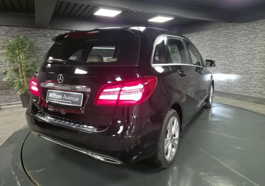 Vue 3/4 arrière droite d'une Mercedes Classe B noire avec feux arrière allumés dans un showroom.