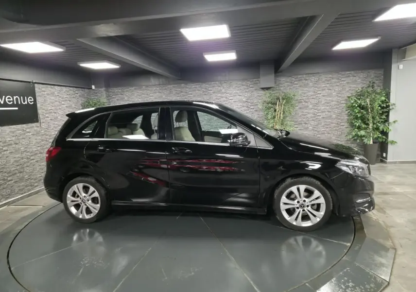 Vue latérale gauche d'une Mercedes Classe B noire 2018 avec jantes alliage 17 pouces dans un showroom.
