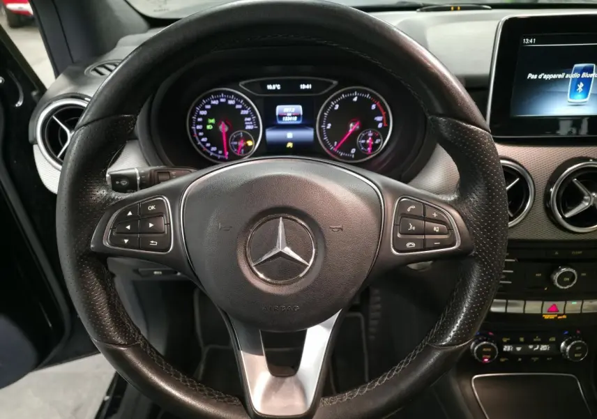 Vue rapprochée du volant cuir noir multifonctions et du tableau de bord digital d’une Mercedes Classe B 180 d 2018.