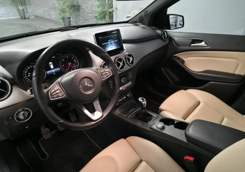 Intérieur de Mercedes Classe B 180 d 2018, vue côté conducteur, sièges beige et volant cuir noir avec commandes multifonctions.
