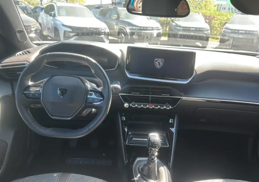 Vue intérieure avant du Peugeot 2008 gris Artense 2025, volant multifonction et écran tactile central allumé au logo Peugeot.