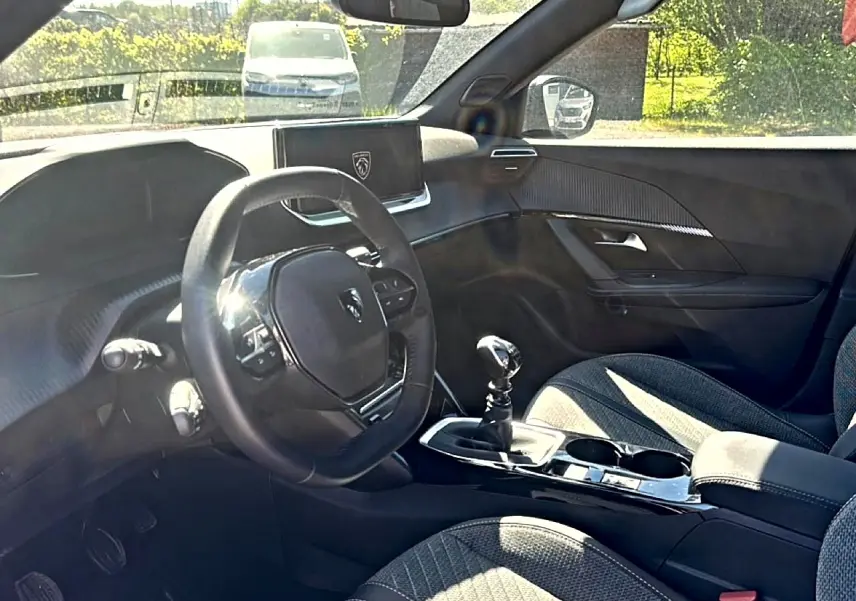 Vue intérieure côté conducteur du Peugeot 2008 1.2 100 Allure 2025, montrant volant compact, écran tactile et sellerie tissu gris.