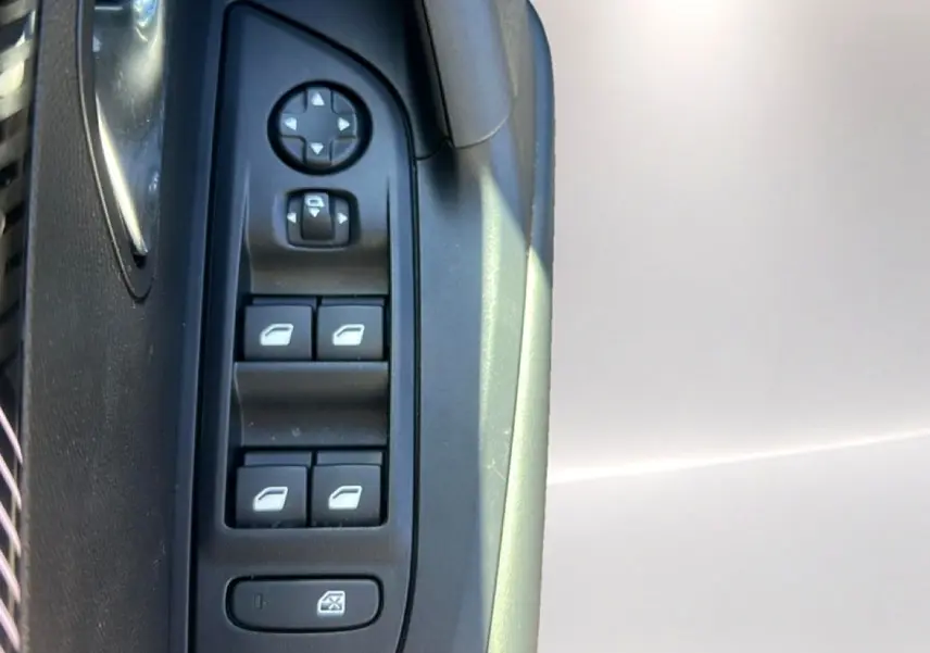 Détail des commandes de lève-vitres et rétroviseurs sur la porte côté gauche d’un Peugeot 2008 gris Artense.