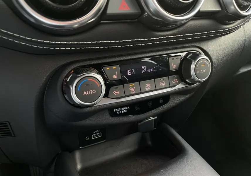 Vue rapprochée de la console centrale noire du Nissan Juke 2024, montrant les commandes de climatisation et sièges chauffants.