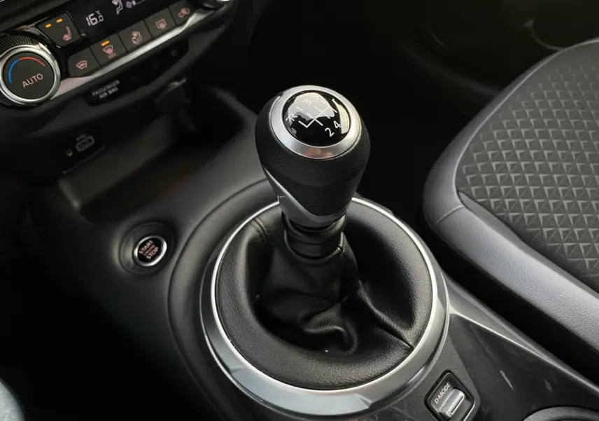 Gros plan sur le levier de vitesses manuel noir et argenté du Nissan Juke blanc perle, avec siège tissu gris à motifs.