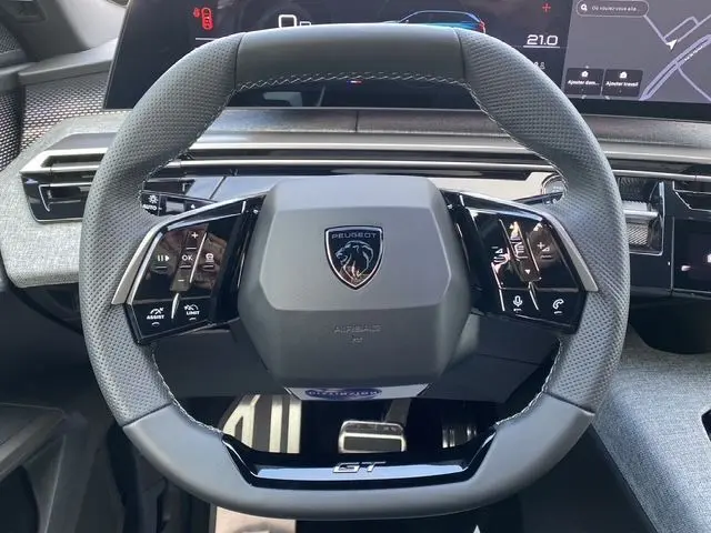 Volant cuir multifonction noir avec logo Peugeot et inscription GT, tableau de bord digital partiellement visible en arrière-plan