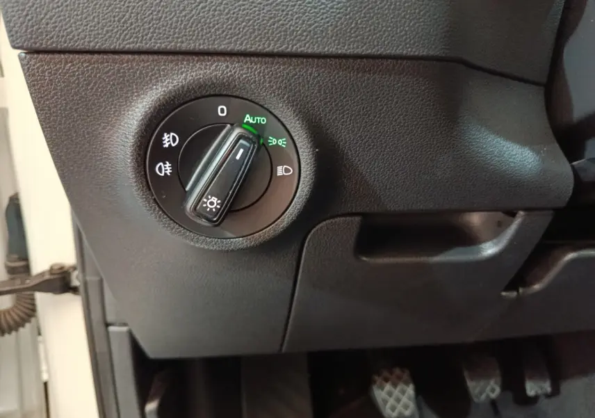 Gros plan sur le bouton de commande des phares en mode automatique, intérieur noir du Skoda Karoq blanc 2024.