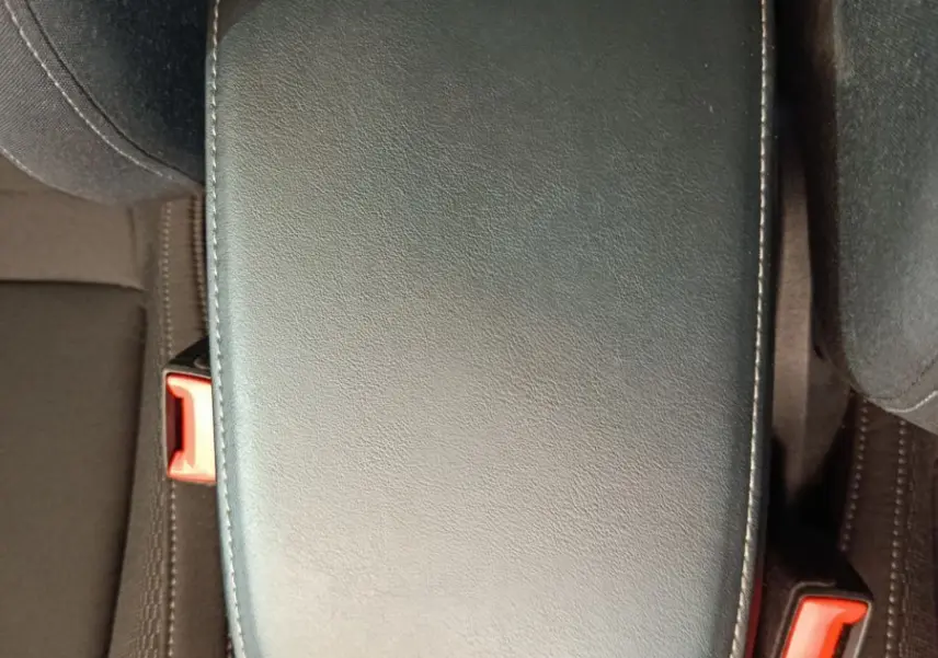 Vue rapprochée de l'accoudoir central noir en cuir entre les sièges avant d'un Skoda Karoq 2024 blanc.