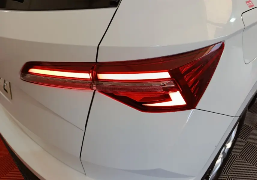 Feu arrière droit allumé sur SKODA KAROQ blanc 2024, vue rapprochée du coffre et porte carburant.
