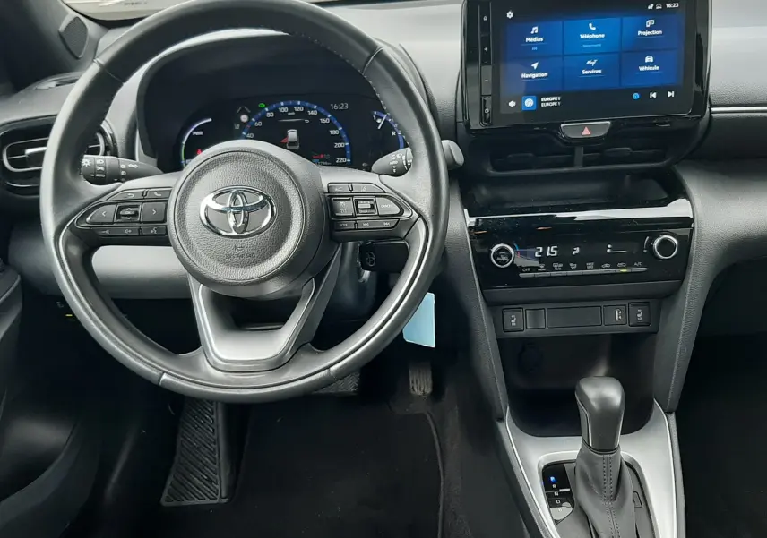 Vue intérieure du poste de conduite de la Toyota Yaris Cross 2024 hybride, avec volant multifonction et écran tactile central allumé.