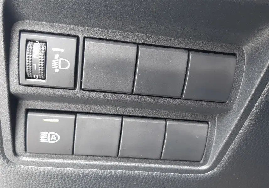 Panneau de commandes intérieures noires avec réglage des phares et bouton d'assistance sur Toyota Yaris Cross 2024.