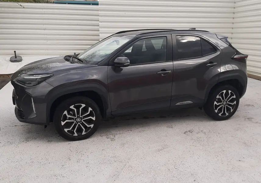 Toyota Yaris Cross gris atlas métal vue de profil côté gauche, avec jantes alliage bicolores et toit noir.