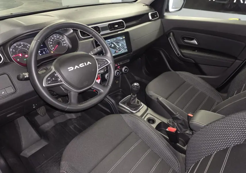 Vue intérieure avant droite du Dacia Duster 2024, tableau de bord noir avec écran tactile et volant multifonction.