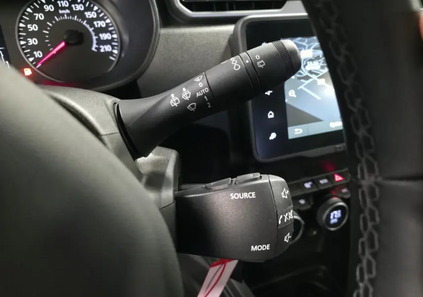 Gros plan sur les commandes au volant noir du Dacia Duster 2024, avec écran tactile et compteur partiel en arrière-plan.