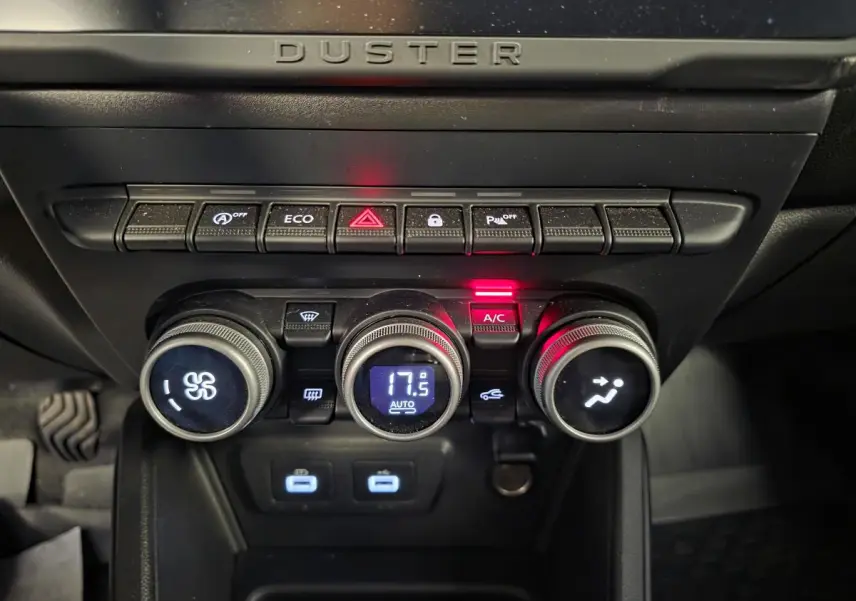 Vue rapprochée de la console centrale du Dacia Duster 2024 avec commandes climatisation automatique et boutons fonctionnels éclairés.