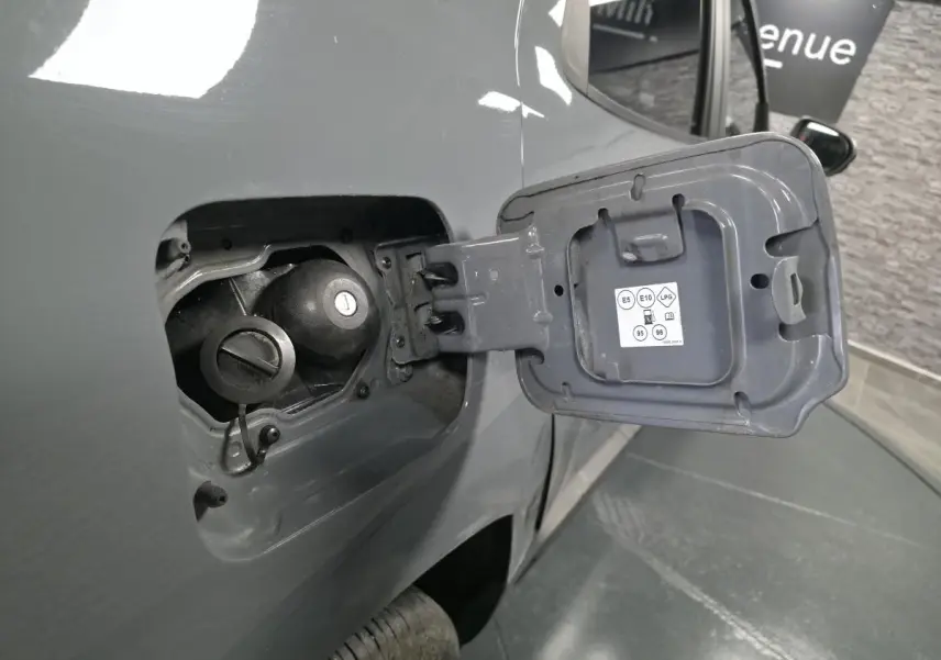 Gros plan sur la trappe à carburant ouverte côté gauche d’un Dacia Duster gris urbain 2024, montrant les bouchons essence et GPL.