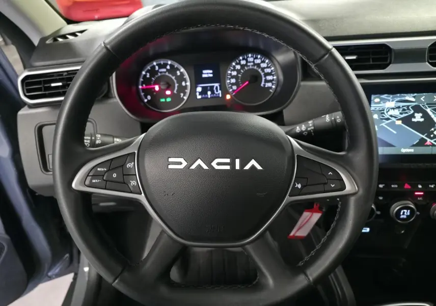 Vue rapprochée du volant noir DACIA avec commandes intégrées et tableau de bord numérique du Duster 2024.