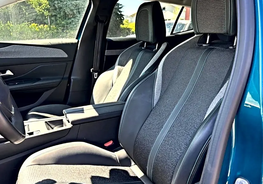 Vue intérieure côté conducteur de la Peugeot 408 Hybrid 145 allure e-dcs6 bleu, sièges tissu et cuir avec accoudoir central.