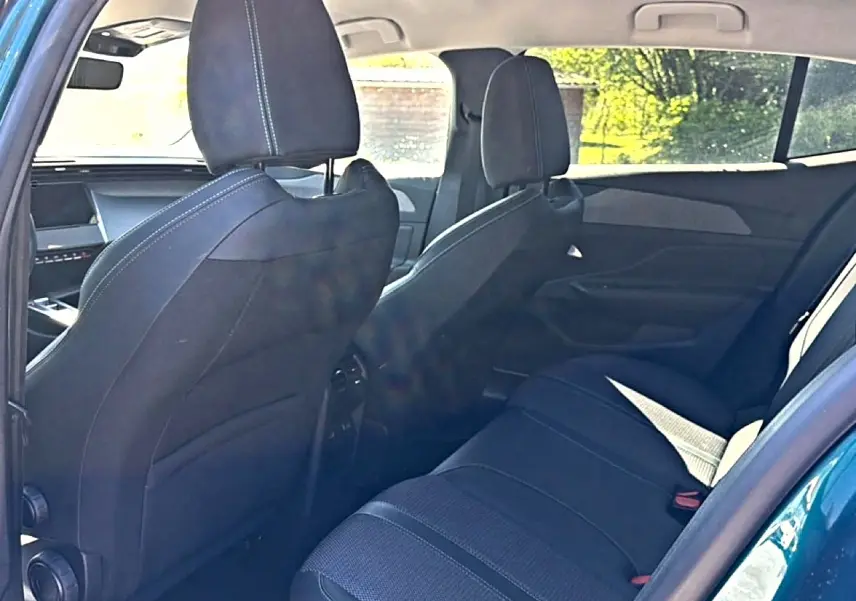 Vue intérieure arrière de la Peugeot 408 Hybrid 145 allure bleu, montrant les sièges arrière et les dossiers avant en tissu noir.