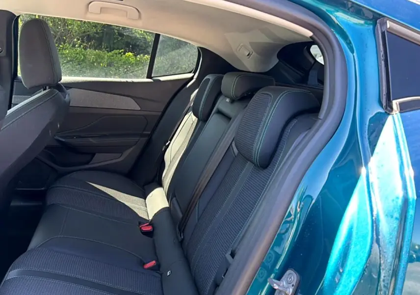 Vue intérieure côté arrière droit d'une Peugeot 408 Hybrid 145 allure e-dcs6 bleu, montrant la banquette arrière en tissu et cuir.