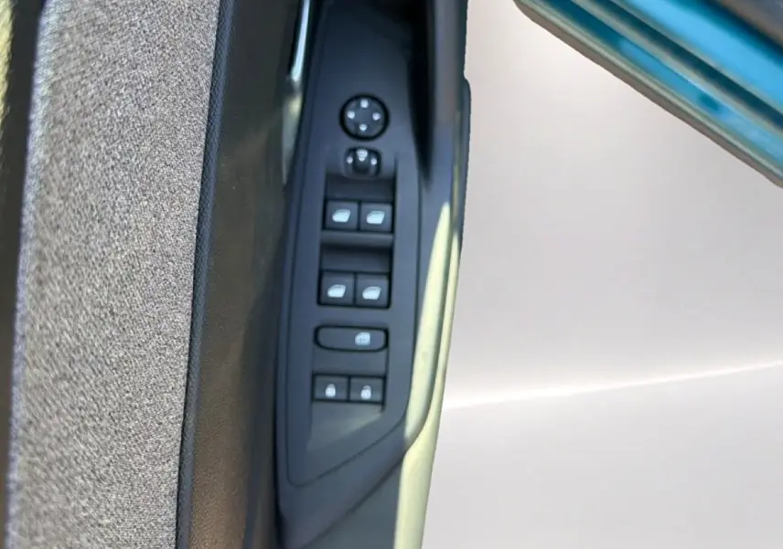 Gros plan sur la commande des vitres électriques côté gauche de la porte d'une Peugeot 408 Hybrid 145 allure bleu 2025.