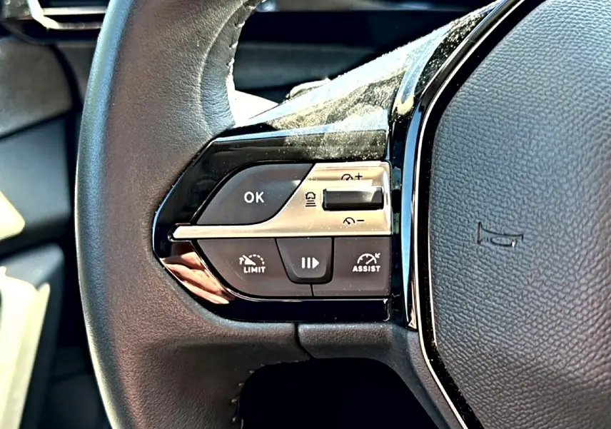 Gros plan sur les commandes gauche du volant cuir noir du Peugeot 408 Hybrid 145 allure 2025.