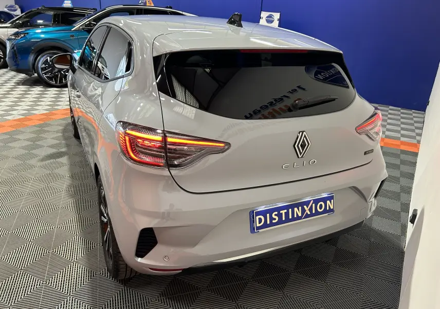 Vue 3/4 arrière droite d'une Renault Clio V gris Rafale avec feux arrière allumés dans un showroom.