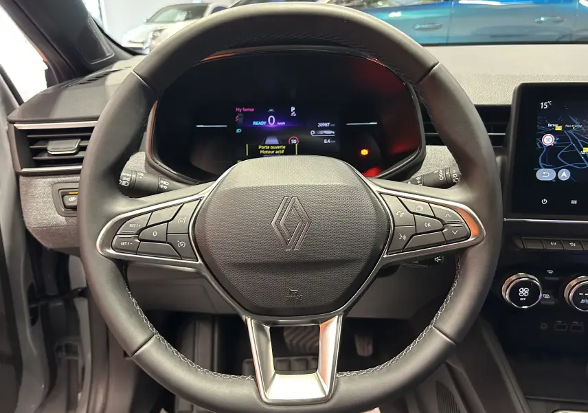 Vue centrée sur le volant noir de la Renault Clio V hybride avec tableau de bord numérique et écran tactile GPS.