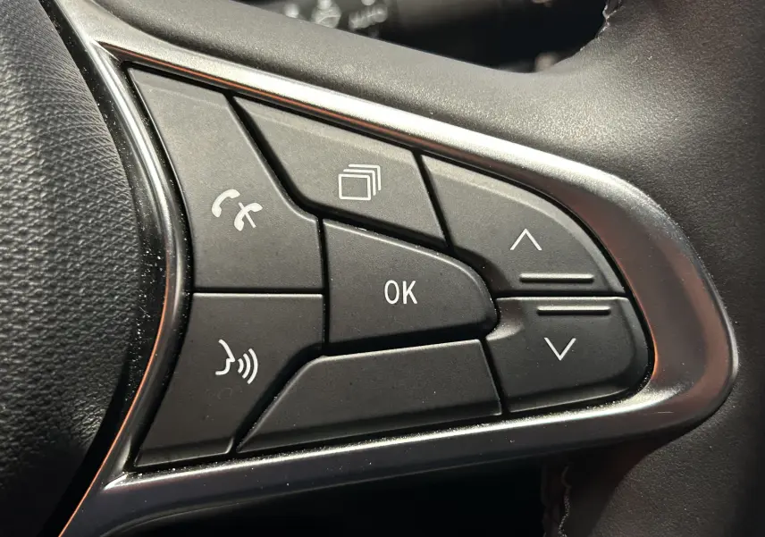Gros plan sur les commandes multifonctions au volant côté gauche de la Renault Clio V hybride, finition gris noir.