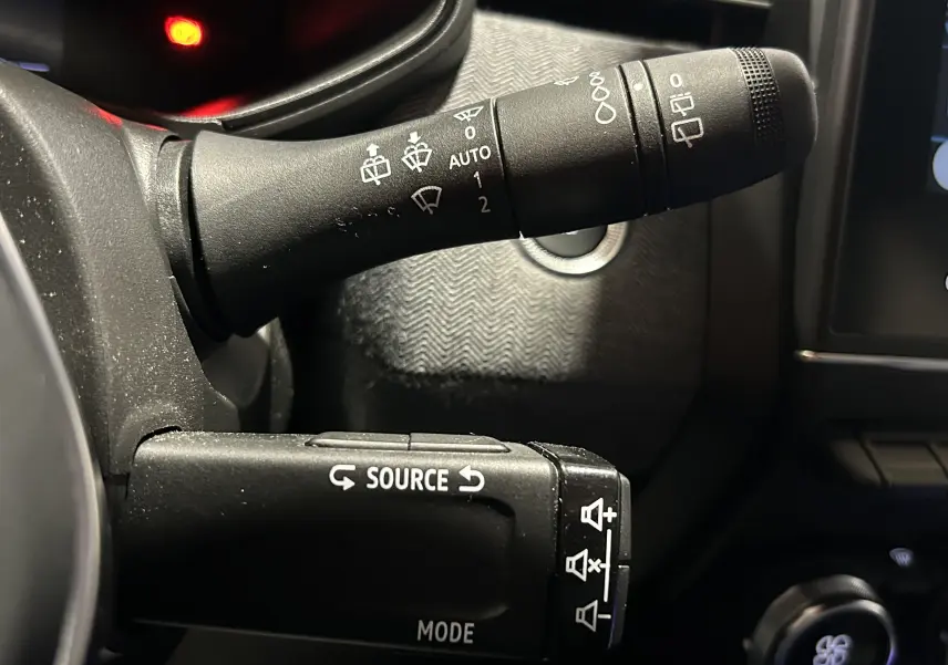 Gros plan sur les commandes de volant noir de la Renault Clio V gris Rafale, avec boutons source et essuie-glace visibles.
