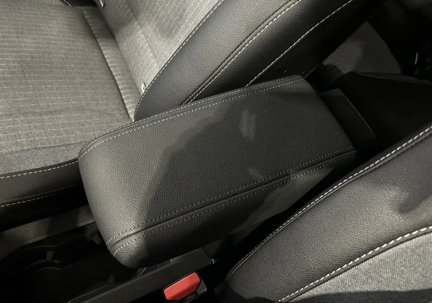 Gros plan sur l'accoudoir central en cuir noir avec surpiqûres blanches, sièges tissu gris et noir Renault Clio V E-Tech.