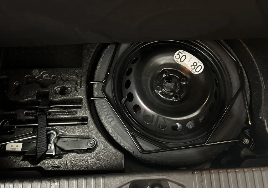 Vue rapprochée de la roue de secours noire et des outils de bord dans le coffre d'une Renault Clio V gris Rafale.