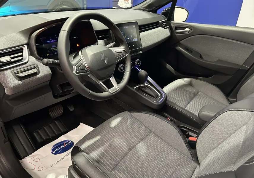 Vue intérieure côté conducteur de la Renault Clio V E-Tech gris rafale, avec tableau de bord digital et sellerie tissu gris.