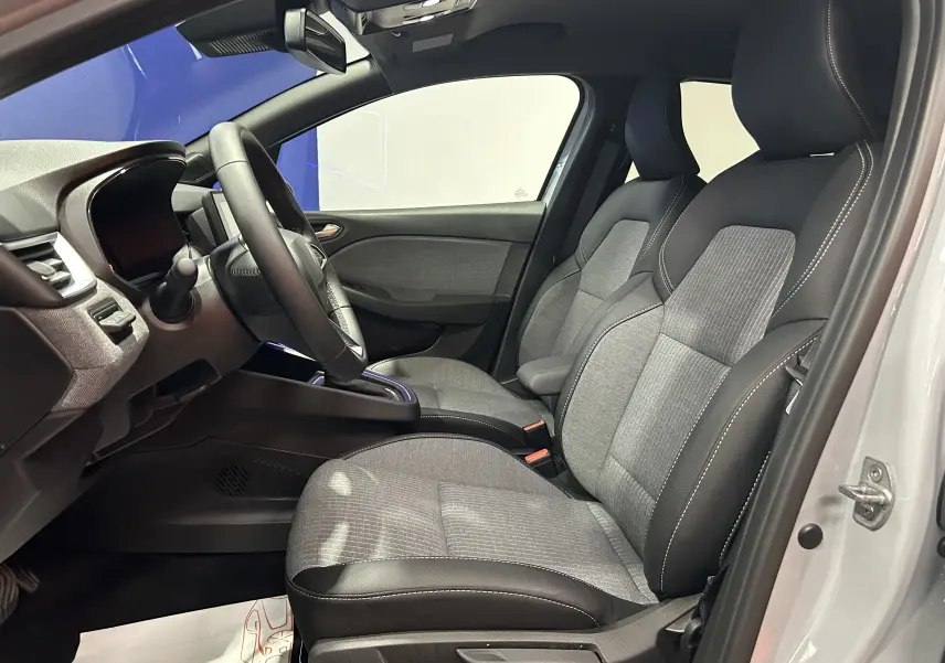 Vue intérieure côté conducteur de la Renault Clio V gris rafale, sièges tissu et cuir gris foncé avec surpiqûres blanches.
