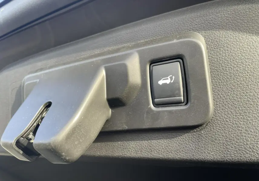 Gros plan sur le bouton d'ouverture du hayon électrique dans un Renault Espace noir étoilé, vue intérieure du coffre.