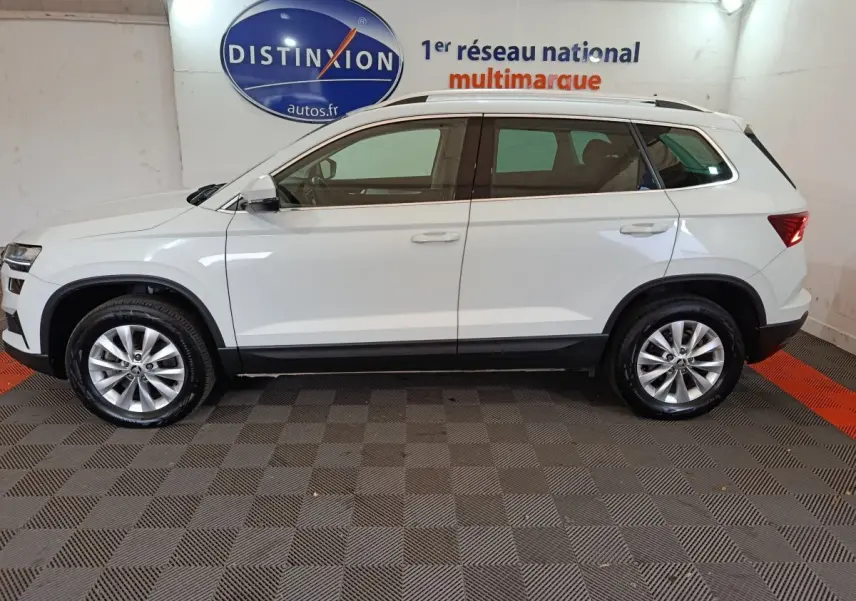 Vue de profil côté gauche d'un Skoda Karoq blanc 2024 avec jantes alliage et barres de toit noires.