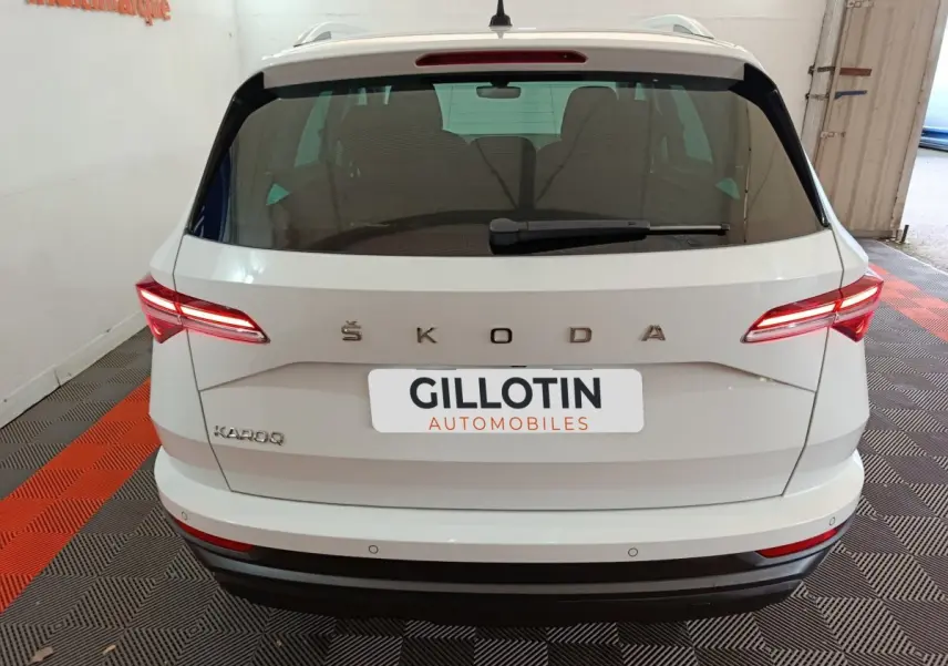 Vue arrière d'un Skoda Karoq blanc 2024 avec feux LED allumés et logo ŠKODA visible sur le hayon.