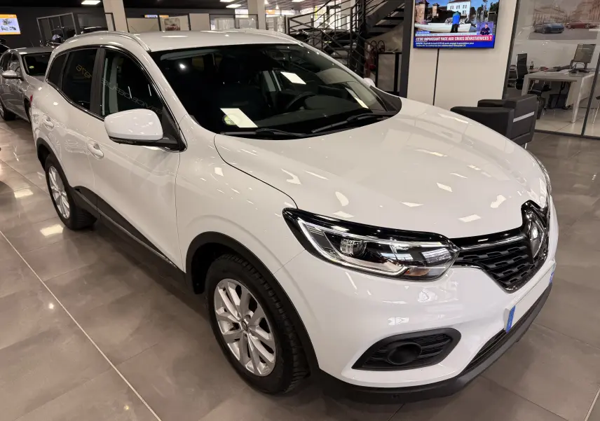 Renault Kadjar blanc Glacier en vue 3/4 avant droit, avec calandre noire et phares LED dans un showroom.