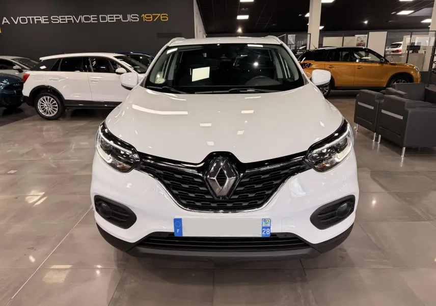 Vue de face d'un Renault Kadjar blanc Glacier 2020 dans un showroom, avec calandre noire et logo Renault bien visible.