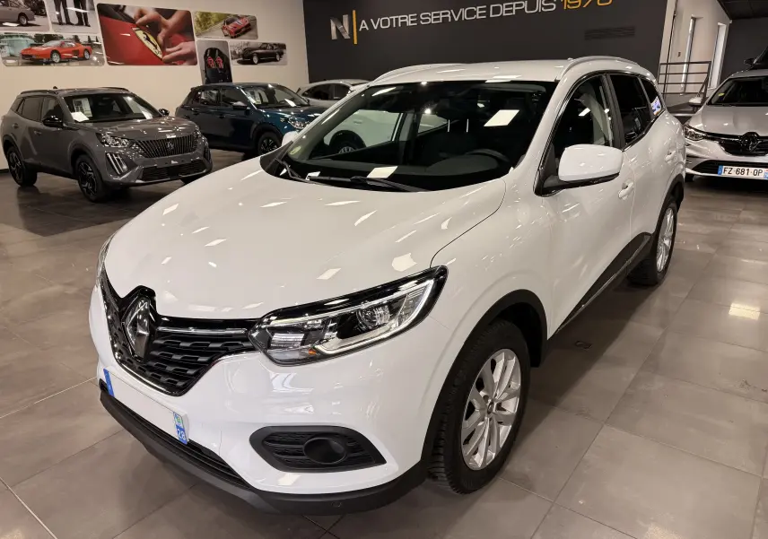 Renault Kadjar blanc Glacier en 3/4 avant droit dans un showroom, avec calandre noire et phares LED visibles.