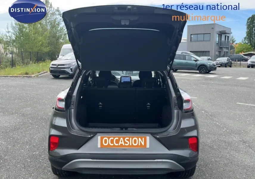 Vue arrière d'un Ford Puma gris 2021 avec coffre ouvert, mettant en valeur les feux arrière et l'espace de chargement.