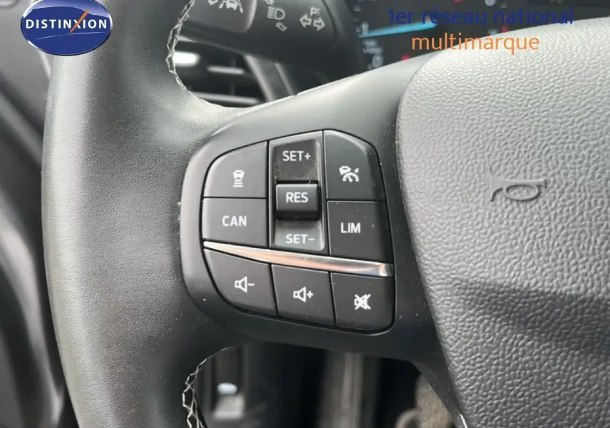 Gros plan sur les commandes du volant noir du Ford Puma gris, montrant les boutons de régulateur et volume sonore.
