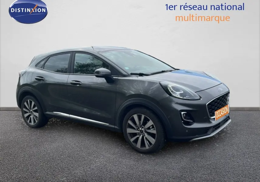 Ford Puma gris en 3/4 avant droit, avec jantes alliage et calandre distinctive, sur fond neutre.