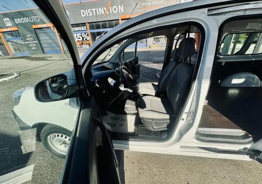 Vue côté gauche avec porte avant ouverte sur l'intérieur gris clair du Renault Kangoo Maxi blanc, montrant les sièges et l'espace de chargement.