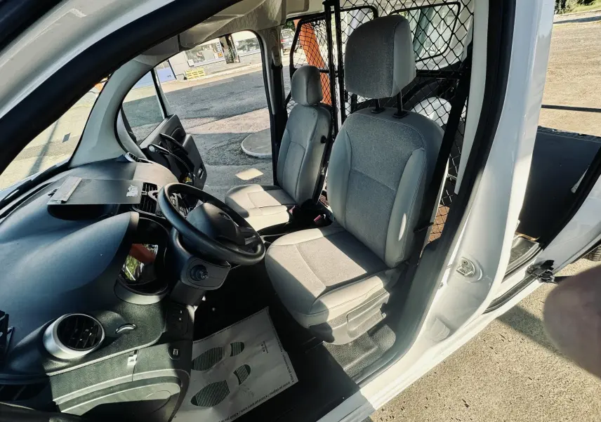 Vue intérieure côté conducteur du Renault Kangoo blanc 2021, montrant les sièges gris et la cloison métallique derrière.