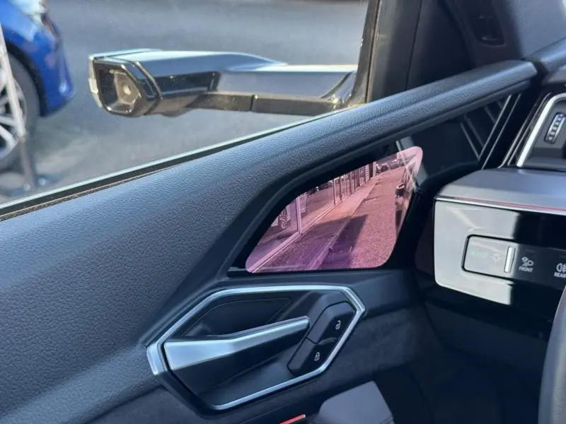 Vue intérieure côté conducteur de l'Audi E-Tron Sportback gris foncé, mettant en valeur le rétroviseur numérique et la poignée de porte.