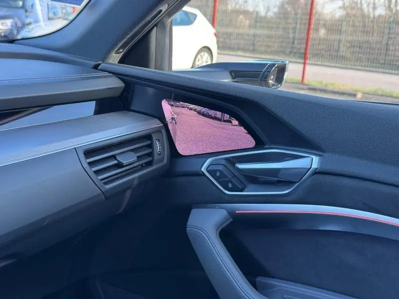 Vue intérieure côté passager de l'Audi E-Tron Sportback gris foncé, mettant en valeur la portière et le rétroviseur digital.