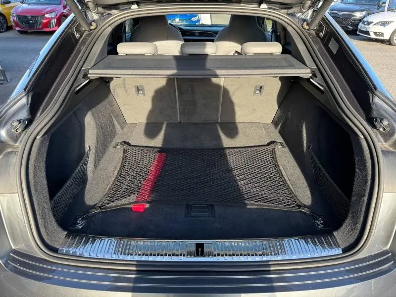 Vue arrière du coffre ouvert d'une Audi E-Tron Sportback gris foncé métal, avec filet de rangement et habillage intérieur noir.